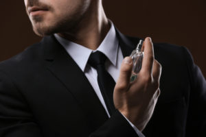 Handsome man in suit using perfume on dark background, closeup